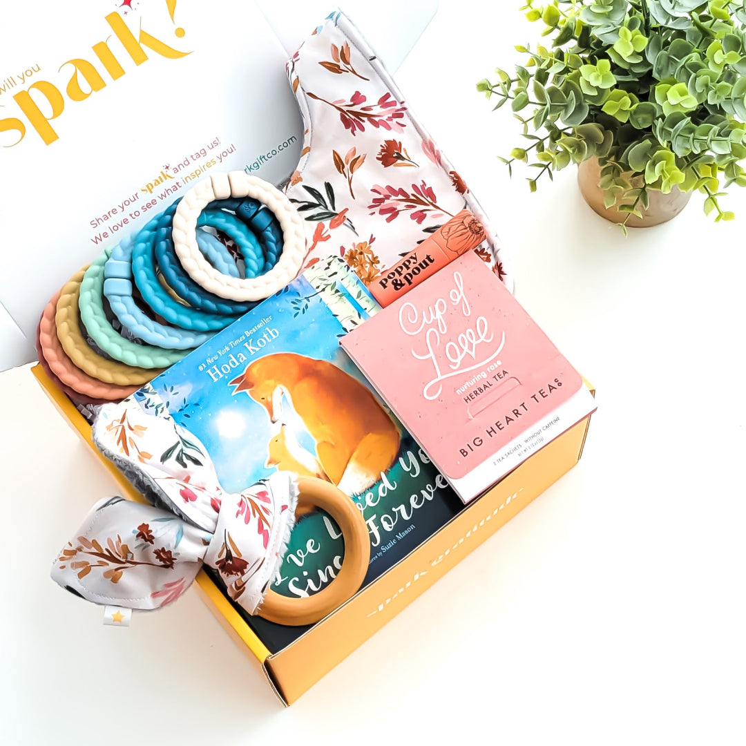 Baby Love Gift Box with a crinkle teether, multi-colored linking rings, autumn garden cloth bib, rose tea sampler, grapefruit lip balm, and optional board book—perfect for baby showers, new parents, and adoption celebrations.