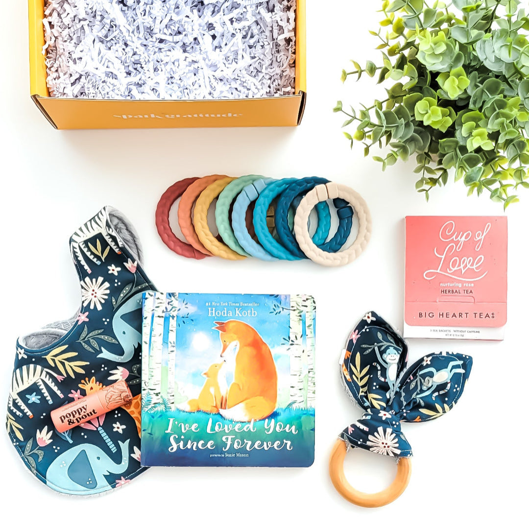 Baby Love Gift Box with a crinkle teether, multi-colored linking rings, jungle love cloth bib, rose tea sampler, grapefruit lip balm, and optional board book—perfect for baby showers, new parents, and adoption celebrations.