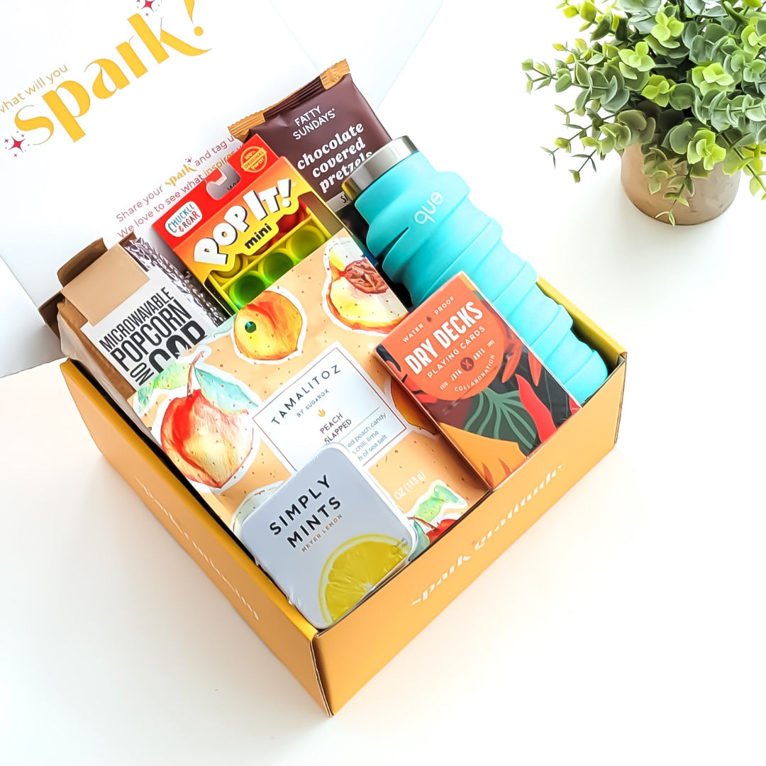 Let’s Play Gift Box featuring a fun game night collection, including microwaveable popcorn on the cob, peach candies, waterproof playing cards, lemon mints, a collapsible water bottle, a mini pop-it, and chocolate-covered pretzels—perfect for friends, family, and game lovers.