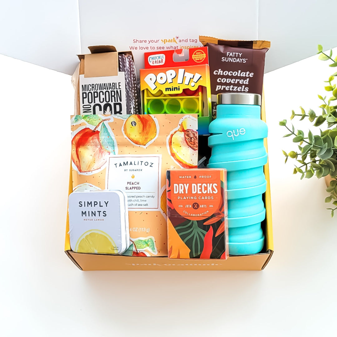 Let’s Play Gift Box featuring a fun game night collection, including microwaveable popcorn on the cob, peach candies, waterproof playing cards, lemon mints, a collapsible water bottle, a mini pop-it, and chocolate-covered pretzels—perfect for friends, family, and game lovers.