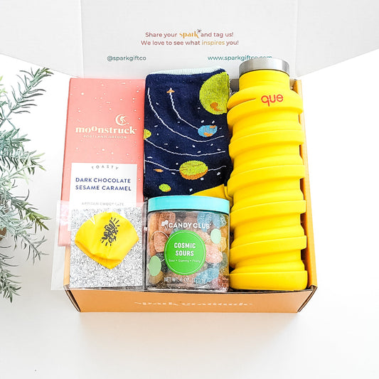 Out of This World Gift Box with space-themed socks, Moonstruck chocolate, cosmic sour candy, a collapsible water bottle, and a space balloon—perfect for galaxy lovers.